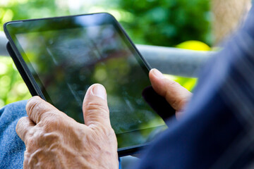 Senior man sitting outside reading E-book on his tablet.