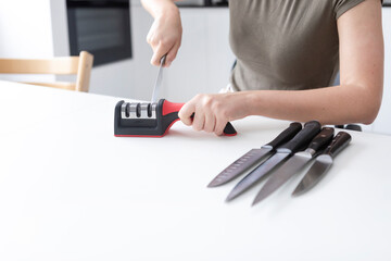 Close-up of woman sharpening knife with special knife sharpener at home	