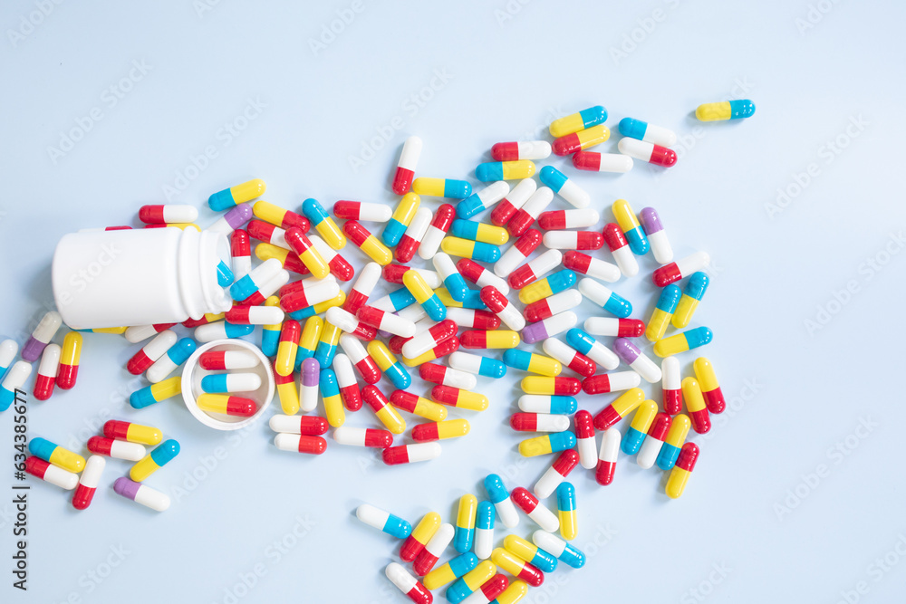 Poster group of assorted color tablets. pills spilling out of white bottle on blue background. top view wit