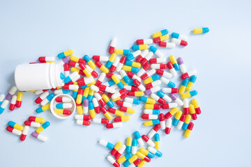 Group of assorted color tablets. Pills spilling out of white bottle on blue background. Top view with copy space for text.