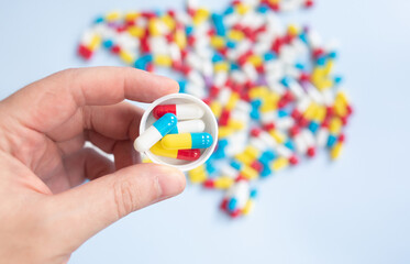 Young guy holding bottle of meds and different pills on light blue background, space for design.