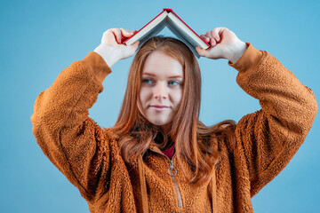 a young woman raised a book above her head in the form of a house, the background is blue