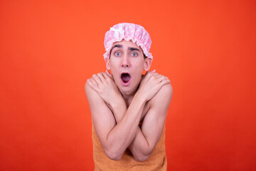 Funny guy in a pink cap poses on an orange background and washes in the shower.