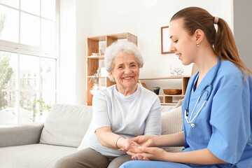 Senior woman with female caregiver holding hands at home