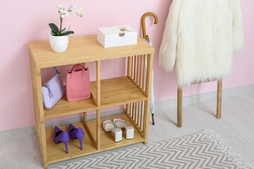 Shelving unit, umbrella and ladder with coat near pink wall in hall