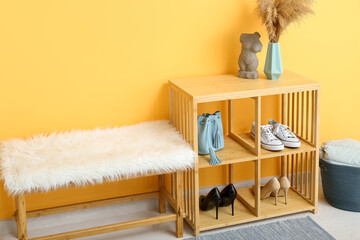 Shelving unit with shoes and bench near orange wall in hall