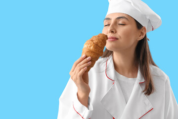 Female chef with tasty croissant on blue background