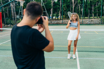 the photographer photographs a blonde model girl on a green tennis court in the form of a tennis player