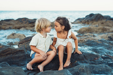 Fototapeta na wymiar blond boy and a brunette girl, three years old, are sitting on stones on the seashore