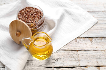 Jug of flax oil and jar with seeds on white wooden background
