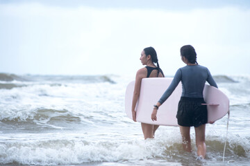Pretty teen girl and her instructor carry a surfboard into the sea, the first lesson to start surfing in the sea, women and outdoor sports