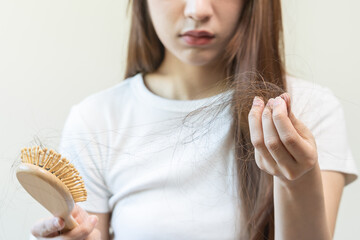 Serious, worried asian young woman, girl holding comb, show her hairbrush with long loss hair problem after brushing, hair fall out problem. Health care, beauty with copy space on white background. - obrazy, fototapety, plakaty