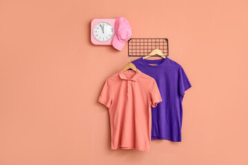 Stylish t-shirts and cap hanging on pink background