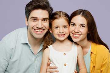 Close up young cheerful cool happy parents mom dad with child kid daughter girl 6 years old wearing blue yellow casual clothes looking camera isolated on plain purple background. Family day concept.