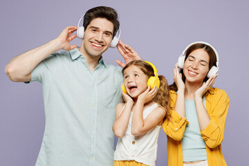 Young fun satisfied parents mom dad with child kid daughter girl 6 years old wear blue yellow casual clothes listen to music in headphones dance isolated on plain purple background Family day concept