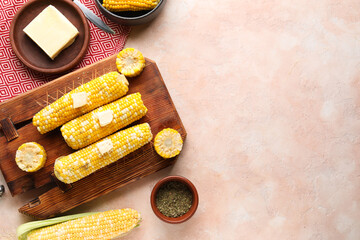 Wooden board of boiled corn cobs with butter on pink background