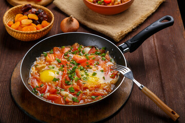 fresh shakshuka in a frying pan sprinkled with green onions on a laid Shabbat table.