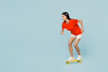 Full body side profile view young fun latin woman she wear orange red t-shirt casual clothes riding pennyboard skateboard isolated on plain pastel light blue cyan background studio. Lifestyle concept.