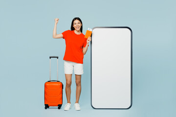 Traveler latin woman wear casual clothes hold suitcase passport ticket big huge blank screen area mobile cell phone isolated on plain blue background. Tourist travel abroad in free time rest getaway.