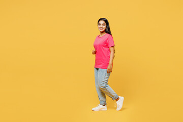 Fototapeta na wymiar Full body side view young smiling fun cheerful happy Indian woman wear pink t-shirt casual clothes walking goign looking camera isolated on plain yellow background studio portrait. Lifestyle concept.