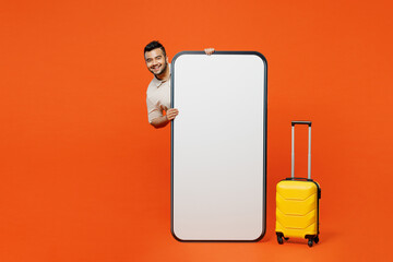 Traveler happy Indian man hold suitcase blank screen mobile cell phone isolated on plain orange red...