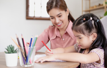 Educational pastime develop creativity skill in kid concept. Asian mother her small daughter in sunny cozy living room, mom teach girl paint use paper and colourful pencils