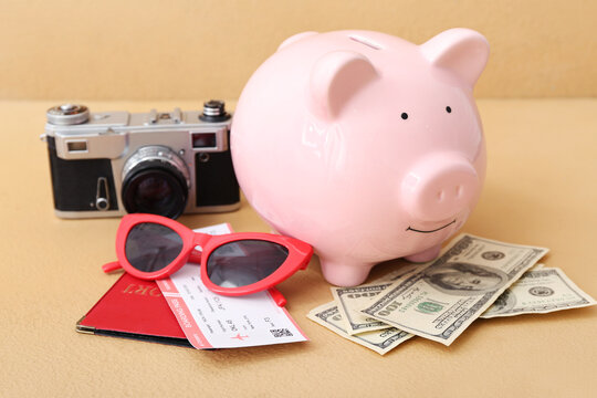Piggy bank with money, photo camera and passport on orange background. Concept of savings for travel