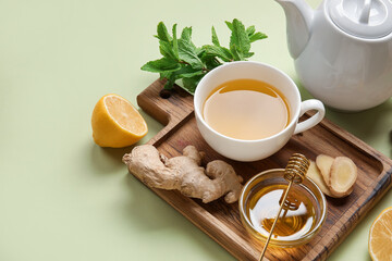 Cup of ginger tea and bowl with honey on green background