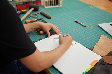 Asian Female Leather worker using pen to make sketch on notebook at the studio 