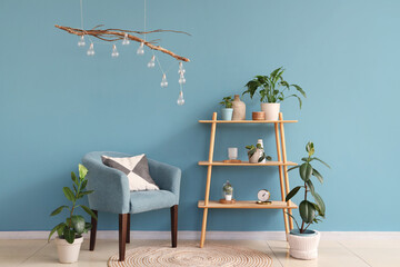 Comfortable armchair, shelving unit and houseplant near blue wall