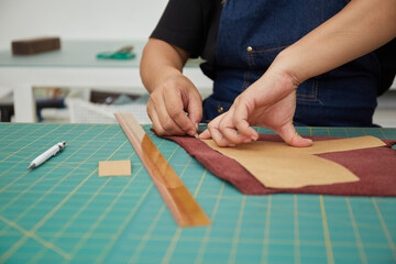 Asian female leather worker tracing pattern on piece of leather

