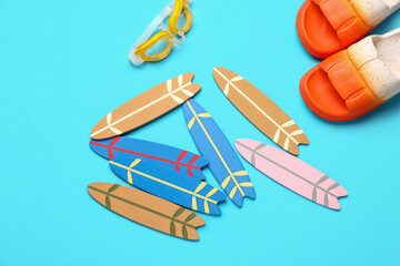 Different mini surfboards, flip-flops and goggles on blue background