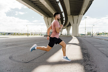 A sporty male athlete training does warm-up exercises. Jogging in the afternoon in the city.  Runner trainer in fitness clothes T-shirt.  Uses a fitness watch.