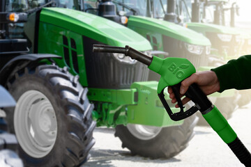 Hand with biofuel refueling nozzle on a background of agricultural tractors.