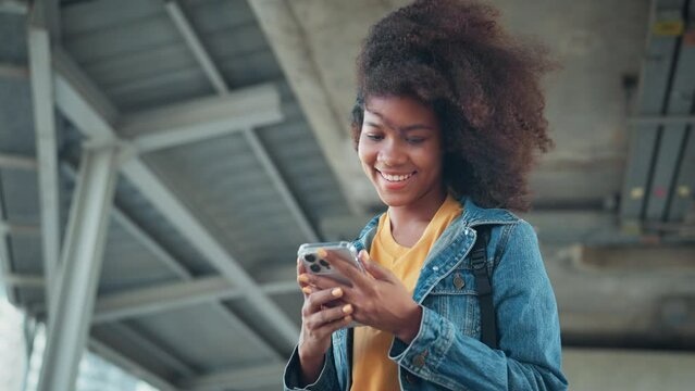 Happy young African American woman using mobile phone with chatting online with friends, Female in jean jacket sitting in the city using social media on smartphone, Technology
