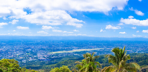 A large city background image with green mountains surrounding it. Panorama, blue sky horizon, lots of white clouds, mountains, airports, villages. Tourist attractions in Thailand.