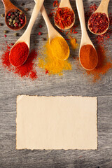 Variety of spices in spoon on table with paper recipe. Food ingredients at kitchen table