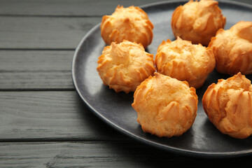 Homemade profiteroles with cream on dark plate on black background. Fresh baked golden profiterole.
