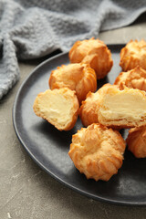 Homemade profiteroles with cream on plate on grey background. Fresh baked golden profiterole. Vertical photo