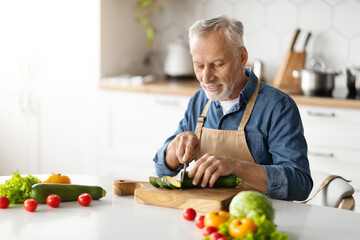 Smiling elderly man in apron cooking vegetable meal in kitchen