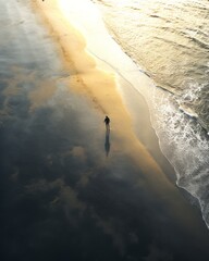 Aerial shot of a distant person walking on the amber colored beach with sunset sky and clouds reflections. Gravity defying northern ocean winter landscape.