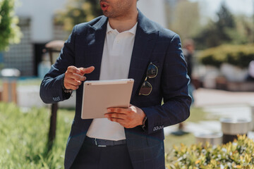 Businessman gestures while holding tablet and explaining something. Cropped photo