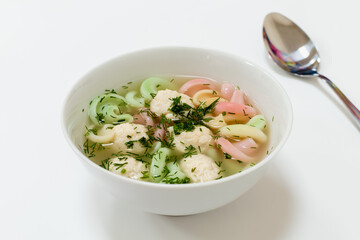 Appetizing light soup with chicken balls, herbs and colored pasta in white plate on white background