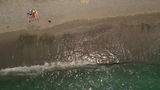 Drone footage of chilling on the sand next to the sunny sea at Paralia Ermones Beach, on a hot day