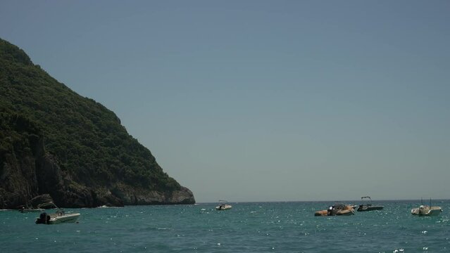 Drone footage of boats gently swaying in the sunny sea, moored not far from the Paralia Ermones Beach, on a hot day