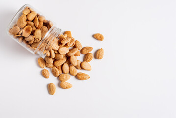Glass jar lying down with fried almonds from inside the jar on a white background,top view.