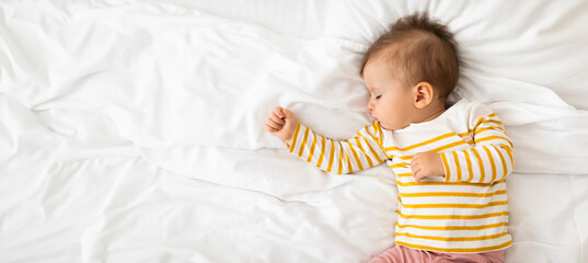 Top view of cute little baby girl napping on bed on white linens during daytime sleep, panorama, free space
