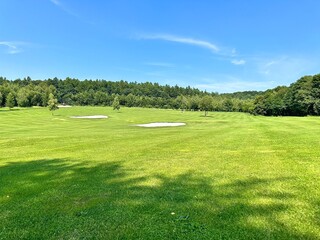 Fototapeta premium Beautiful golf course with hills, sand and trees. A view of the green lawn of the golf course.