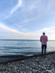 A young man in a panama hat stands on the seashore