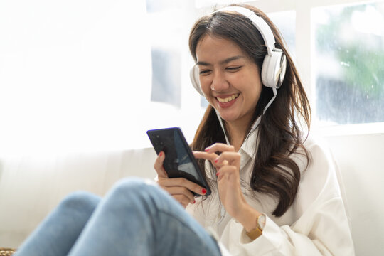Happy young asian woman relaxing at home.Female smile sitting on floor and holding mobile smartphone at home.Listening to music on lazy and relax day at summer 